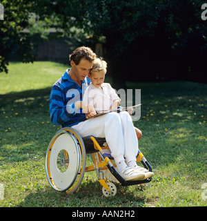 Behinderter im Rollstuhl liest einem kleinen Jungen im Garten ein Buch vor Stockfoto