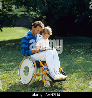 Behinderter im Rollstuhl liest einem kleinen Jungen im Garten ein Buch vor Stockfoto