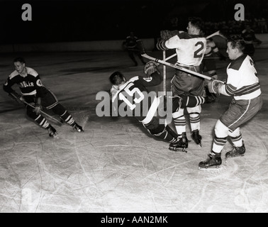 1950ER JAHRE EISHOCKEY-SPIEL MIT EINER DER 4 SPIELER IM VORDERGRUND WIRD ABGERISSEN DURCH 2 MITGLIEDER DES GEGNERISCHEN TEAMS Stockfoto