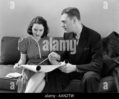 1940ER JAHREN PAAR SITZT AUF DER COUCH BETRACHTEN BLAUPAUSEN Stockfoto