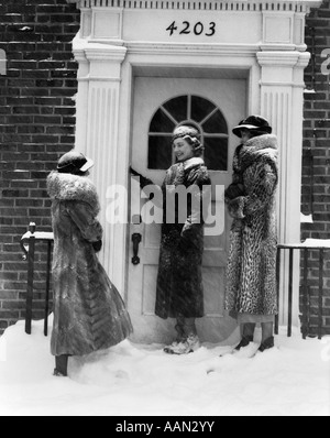 1930ER JAHREN 3 FRAUEN PELZ MÄNTEL RING TÜR BELL BACKSTEINGEBÄUDE SCHNEE Stockfoto