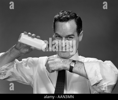 1950ER JAHRE MANN, DER BABY-FLASCHE MILCH CHECK-TEMPERATUR AUF HAND LÄCHELNDEN BLICK IN DIE KAMERA HÄLT Stockfoto