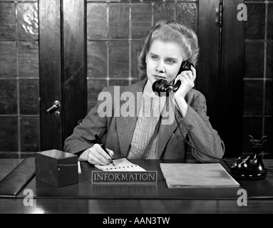 1940ER JAHRE JUNGE FRAU SITZT AM INFORMATION DESK SEKRETÄR GESPRÄCH AM TELEFON SCHREIBEN Stockfoto