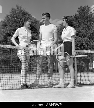 1940S 1950S KERL ZWEI MÄDCHEN UND EIN TENNISSPIELER MIT TENNISSCHLÄGER UND TENNISBALL STEHEN IN DER NÄHE VON NET Stockfoto