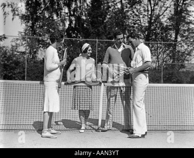 1930S 1920S TENNIS DOPPEL ZWEI MÄDCHEN ZWEI JUNGEN TENNISPLATZ SCHLÄGER STEHEN IN DER NÄHE VON NET FESTHALTEN Stockfoto