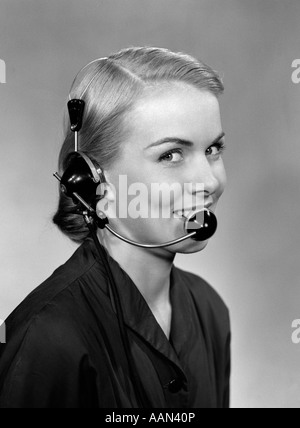 1950ER JAHRE 3/4 PROFILBILDNIS DER ANGESTELLTE AN DER REZEPTION TRAGEN HEADSET BLICK IN DIE KAMERA LÄCHELN Stockfoto