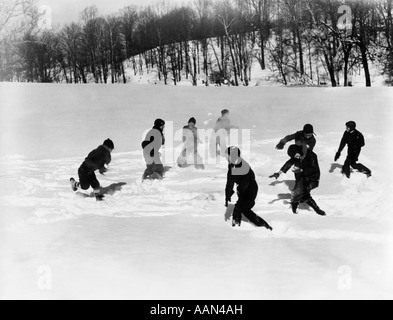 1930ER JAHRE GRUPPE 8 JUNGEN ZWEI VIERER-TEAMS HABEN EINE MASSIVE SCHNEEBALLSCHLACHT IM SCHNEE ÜBERDACHTEN BEREICH Stockfoto