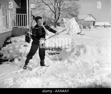 1950ER JAHREN KÄMPFEN HART ARBEITENDE FRAU SCHAUFEL SCHNEE VOM GEHSTEIG BAUERNHAUS MIT VERANDA Stockfoto