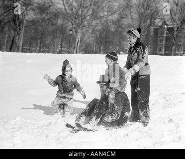 1930ER JAHRE GEKLEIDET MANN & FRAU MIT EINEM JUNGEN & MÄDCHEN IN WINTERKLEIDUNG MIT SCHLITTEN IN SCHNEEBEDECKTEN FELD SPIELEN Stockfoto