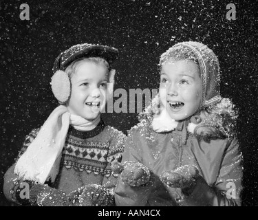 1950ER JAHREN GEHÖRSCHUTZKAPSELN JUNGE MÄDCHEN IM WINTER KLEID MÜTZEN HANDSCHUHE OHR SCHAL LÄCHELT GLÜCKLICH DEKOSCHNEE FLOCKEN FALLEN STUDIOAUFNAHME Stockfoto