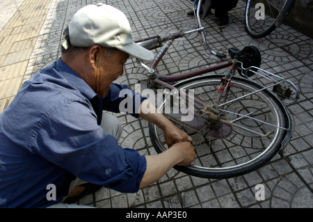 China Shanxi Datong Mann den Schlauch Reifen eines Fahrrades auf dem Bürgersteig zu reparieren Stockfoto