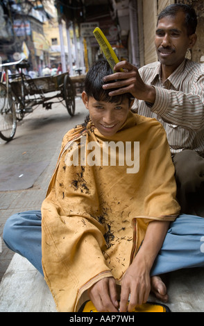 Ein Barbier, geben einen neuen Haarschnitt zu einem Client auf einer Straße in einem Markt, Chandni Chowk, New Delhi, Indien Stockfoto