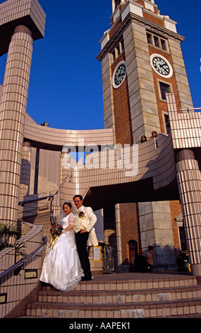 Braut und Bräutigam posiert neben Uhrturm, Hong Kong Cultural Centre, Kowloon, Hong Kong, China. Abendlicht Stockfoto