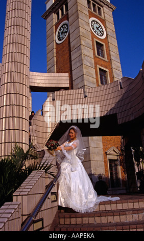 Braut posiert neben Uhrturm, Hong Kong Cultural Centre, Kowloon, Hong Kong, China. Abendlicht Stockfoto