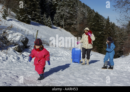 Eine Frau mit zwei Kindern zu Fuß auf einem verschneiten Pfad mit einem Schlitten Stockfoto