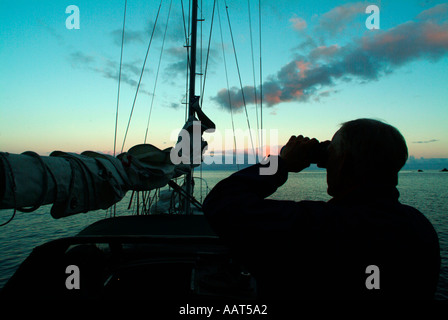 Ein Matrose auf einem Ozean-Passage sucht den Horizont mit dem Fernglas vom Deck sein Segelboot. Vielleicht sucht er nach land Stockfoto