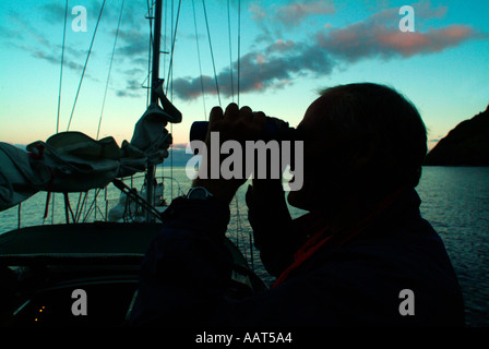 Ein Matrose auf einem Ozean-Passage sucht den Horizont mit dem Fernglas vom Deck sein Segelboot. Vielleicht sucht er nach land Stockfoto
