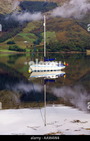 Weißes Segel Boot vor Anker am Loch Leven in der Nähe von Ballachulish Glencoe mit leichten Wolken treiben durch die bergige Kulisse Stockfoto