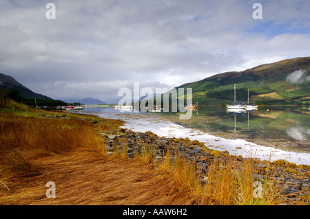 Boote am Loch Leven am Balluchullish mit grasbewachsenen Felsenküste im Vordergrund und perfekte Spiegelungen in der Oberfläche des Wassers Stockfoto