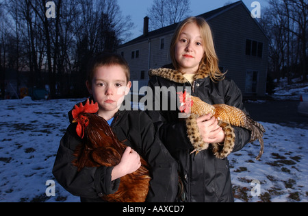 Ein kleiner Junge und Mädchen holding Hähne Hühner Hühner als ihr Haustier vor Haus Stockfoto