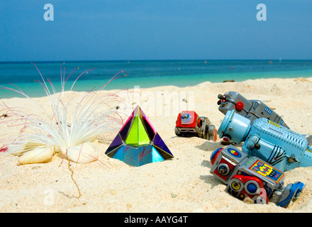 Vier Spielzeugroboter Verehrung einer Glaspyramide an einem tropischen Strand Stockfoto