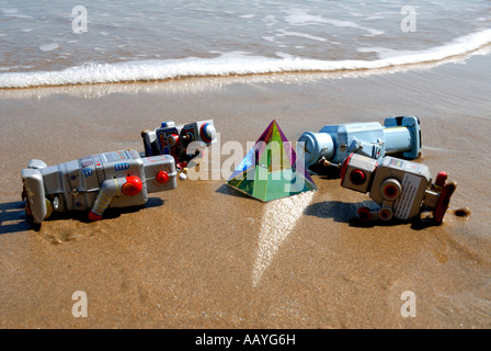 Vier Spielzeugroboter Verehrung einer Glaspyramide auf einem englischen Strand Stockfoto