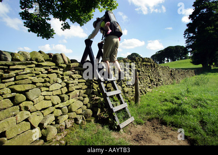 Eine Frau mit einem Kind in einem Rucksack-Träger klettert einen Stil während des Gehens der Yorkshire Dales Weg, England, UK Stockfoto