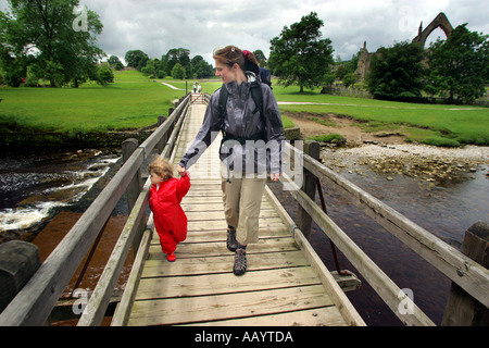Eine Frau und ein kleines Kind überqueren eine Brücke bei Bolton Abbey Ruinen während des Gehens der Dales Weg in Yorkshire, Großbritannien Stockfoto