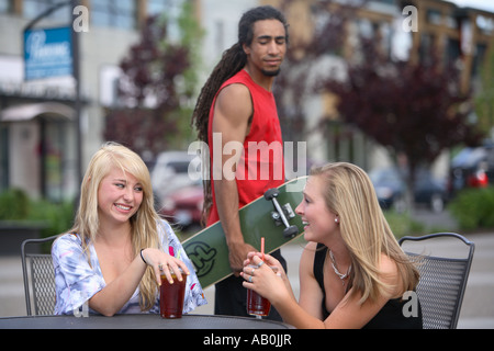 Zwei Mädchen im Gespräch mit Kerl im Hintergrund prüfen sie aus Stockfoto