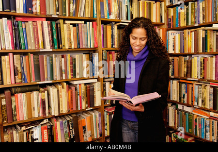 Frau in Buchhandlung am Hay on Wye Powys Wales UK mit gebundene Bücher in den Regalen stöbern und sich mit Blick auf offenes Buch Stockfoto