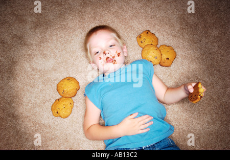 Kind, die Verlegung auf Teppich mit Schokolade auf Gesicht und Cookie in der hand Stockfoto