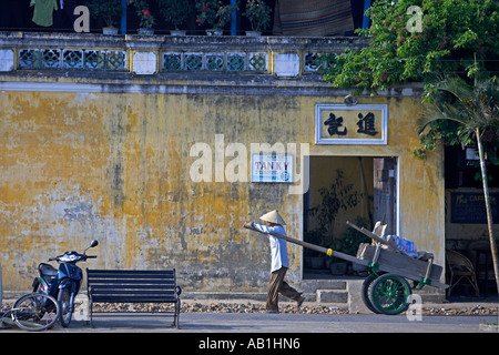 Mann mit konischen Hut zieht Handwagen entlang Straße Hoi an einer historischen Stadt Mitte Vietnam Stockfoto