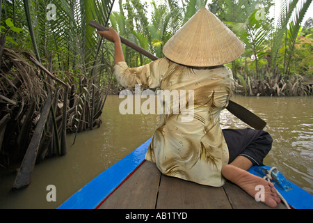 Frau in konische Hut Paddlling Boot durch die Backwaters und Palmen Vietnam Mekong Delta Stockfoto