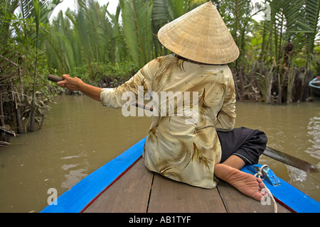 Frau in konische Hut Paddlling Boot durch die Backwaters und Palmen Vietnam Mekong Delta Stockfoto