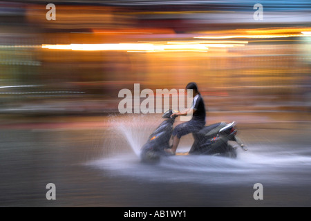 Junge Frau fährt Motorroller mit Geschwindigkeit im Regen entlang überflutet De Tham Street Pham Ngu Lao Bezirk Ho Chi Minh City, Vietnam Stockfoto