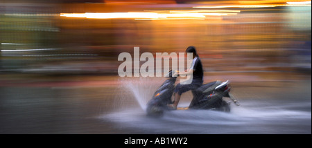 Junge Frau fährt Motorroller mit Geschwindigkeit im Regen entlang überflutet De Tham Street Pham Ngu Lao Bezirk Ho Chi Minh City, Vietnam Stockfoto