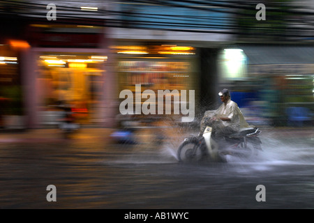 Mann im Cape auf Motorrad fährt Regen entlang überflutet De Tham Street Pham Ngu Lao Bezirk Ho Chi Minh City, Vietnam Stockfoto