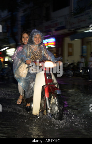 Zwei Frauen in Kunststoff Regen-Capes fahren Motorrad entlang überflutet De Tham Street Pham Ngu Lao Bezirk Ho Chi Minh City, Vietnam Stockfoto