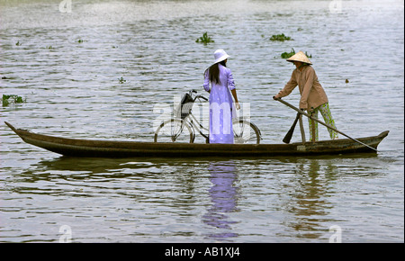 Frau in konische Hut Paddlling Frau in Ao Dai mit Fahrrad in Fähre über den Fluss Mekong Delta Vietnam Stockfoto