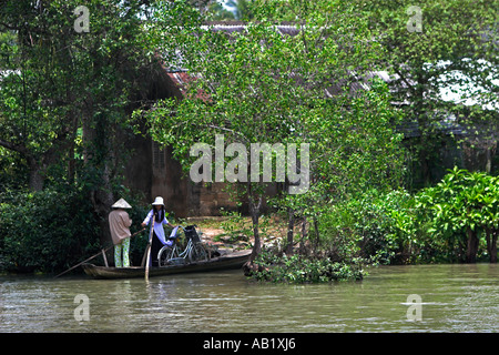 Frau in konische Hut nimmt Tarif für Paddlling Frau und Fahrrad mit einer Fähre über Fluss Vietnam Mekong Delta Stockfoto