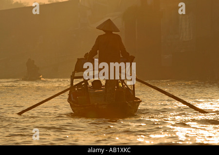 Frau in konische Hut steht Fluss Tretboot in Sunrise Cai Ran schwimmenden Markt in der Nähe können Tho Vietnam Stockfoto