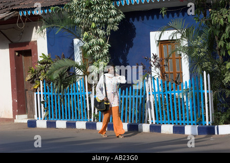 Frau geht vorbei an leuchtend blauen Haus im Kolonialstil inmitten tropischer Pflanzen in Fontainhas Bezirk von Panjim Goa Indien Stockfoto