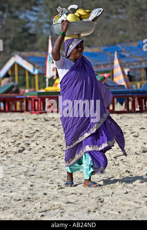 Frau in lila Sari mit Obst aus Schüssel trug auf dem Kopf Cavelossim Beach Goa Indien Stockfoto