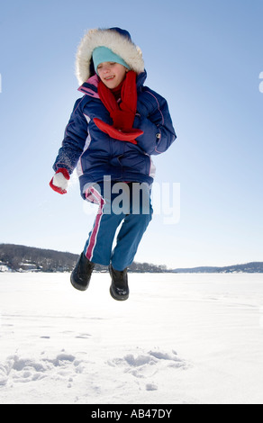 Ein junges Mädchen springt auf einem zugefrorenen See mit Schnee bedeckt Stockfoto