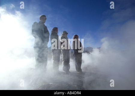 Vier Touristen Semi Silhouette unter Dampf aus bei El Tatio Geysire in der frühen Morgensonne. Stockfoto