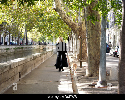 blonde Frau mit Hund zu Fuß durch einen Kanal in Nimes, Frankreich. Stockfoto