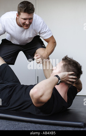 ein junger Mann dabei Sit up Übung und ein Freund ihn anfeuern Stockfoto