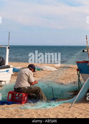 Armacao de Pera Algarve Portugal Fischer Flicken sein Netz neben seinem hölzernen Angeln Boot am Sandstrand Stockfoto