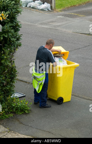 Blick auf den Straßenbelag von Residential Street auf den müllsammler des stadtrats, der ein Haus aus recycelbarem Papier aus einer Kunststoffbox in einen gelben Müllcontainer UK transportiert Stockfoto