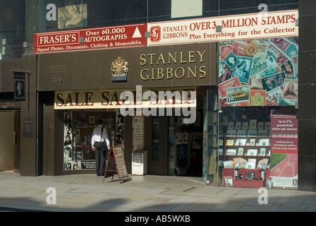 Der Strand Stanley Gibbons Briefmarkenladen mit einem Mann, der auf die Schaufensterauslage schaut, und Royal Warrant mit Philadelphia Illustrationen London England UK Stockfoto